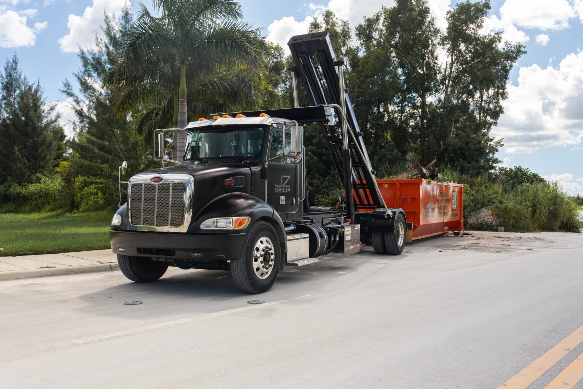 JZ hauling truck with its roll-off lifting mechanism raised beside an orange container